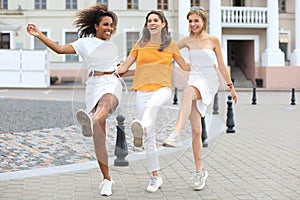 Three young smiling hipster women in summer clothes posing on street.Female showing positive face emotions. Dancing