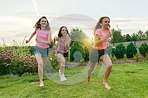 Three young sports girls teenagers running on a green lawn against the backdrop of summer sunset.