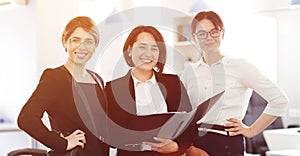 Three young successful business women in the office smiling happily