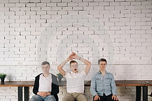 Three young tired guys sitting against a white brick wall waiting for something important.