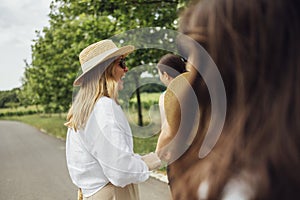 Three young women in casual clothes and with straw hats are joyfully running along the path in the park