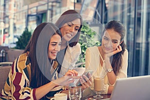 Three young women at coffee break using smart phone.