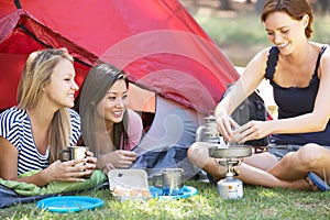 Three Young Women Cooking On Camping Stove Outside Tent