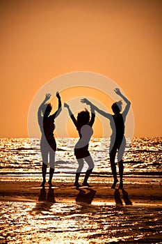 Three Young Women Dancing On Beach At Sunset