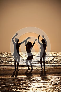 Three Young Women Dancing On Beach At Sunset