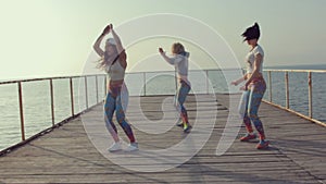 Three young women dancing twerk on a wooden pier near the sea