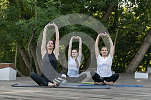 Three young women do exercises on outdoors. Yoga practice in the morning in park. Balance and harmony. Breathing practices