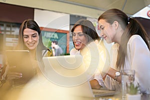 Three young women having conversation in cafe using lap top and