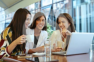 Three young women having conversation in cafe and using laptop.