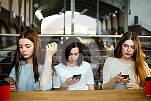 Three young women typing messages on smart phones