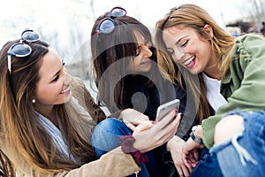 Three young women using a mobile phone in the street.