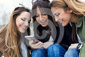 Three young women using a mobile phone in the street.