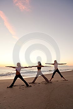 Three Women Practicing Yoga on Beach At Sunrise or Sunset