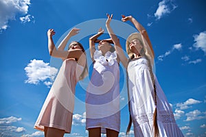 Three young women in white dress posing against the blue sky in a wheat field