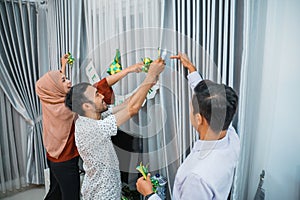 three youngsters decorate for eid mubarak celebration on curtains