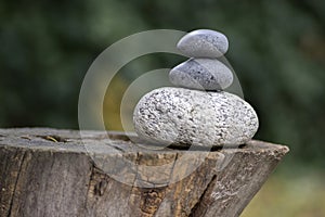 Three zen stones pile on wooden stump, white and grey meditation pebbles tower