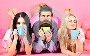 Threesome relax in morning with coffee. Lovers concept. Man and women, friends on sleepy faces lay, pink background. Man