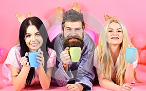 Threesome relax in morning with coffee. Lovers concept. Man and women, friends on smiling faces lay, pink background