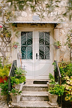 Threshold of an old stone house with a wooden door with a forged lattice and flowers in pots