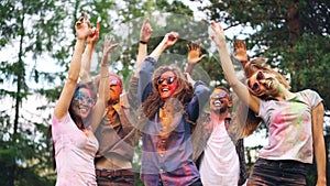 Thrilled men and women are dancing having fun at modern party, their faces and clothes are covered with multicolor paint