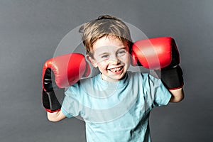 Thrilled young boy giggling with boxing gloves up for fight