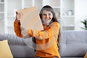 Thrilled young eastern woman holding cardbox parcel, home interior