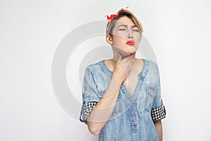 Throat pain or cold. Portrait of sick young woman in casual blue denim shirt with makeup and red headband standing and holding her