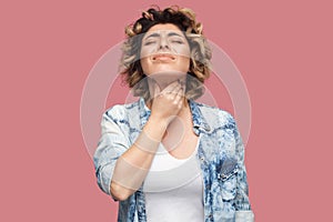 Throat pain or cold. Portrait of young woman with curly hairstyle in casual blue shirt standing and holding her painful neck