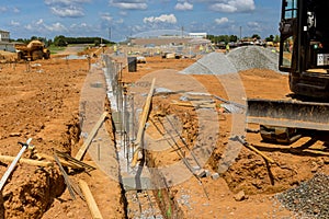 Throughout the construction site, steel bars and rebar wires have been placed into the trench to reinforce the concrete