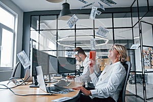 Throwing money to the air by special device. Two stockbrokers in formal clothes have a break and fun in the office