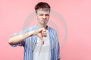 Thumb down, I don`t like it. Portrait of upset displeased brown-haired man showing dislike gesture. isolated on pink background