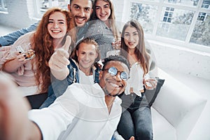 Thumb up. Cheerful young friends having fun and drinking in the white interior