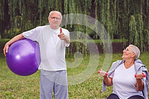 thumb up for healthy exercising - Happy senior couple with fitness balls in park.