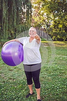 thumb up for healthy exercising - Happy senior woman with fitness balls in park.