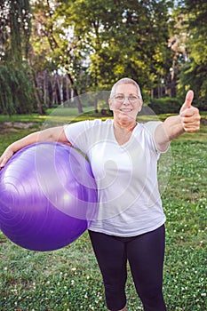 thumb up for healthy exercising - Smiling senior woman with fitness balls in park.