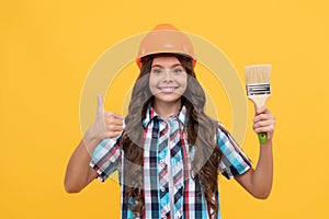 thumb up for success. happy teen girl hold painting brush. child painter in helmet.