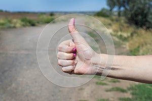 Thumb up is the symbol or sign of help or favor or hitchhike from hitchhiker on a road. Woman is showing her thumb for hitchhiking