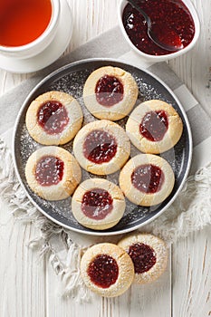 Thumbprint Christmas cookies filled with raspberry jam closeup on the plate served with tea on the wooden table. Vertical top view