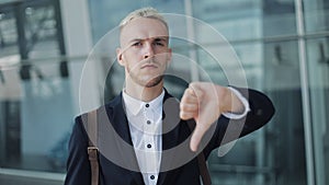 Thumbs Down by Young Attractive Businessman Outside Office. Happy Man Standing near Airport and Looking into the Camera