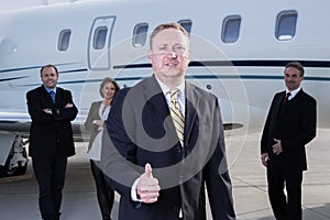 Thumbs up business team in front of corporate private jet