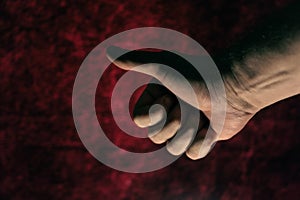 A thumbs up gesture. Hand of a mature man against a dark red background. Close-up. Selective focus. Defocus, noise, grain effect