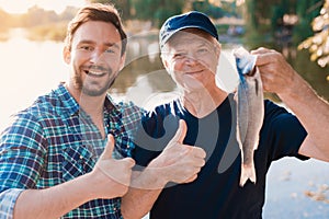 Thumbs up. A man stands next to an old man who is holding a fish he has just caught