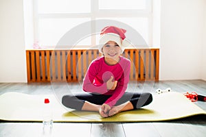 Thumbs up Merry Christmas and a happy new year Little girl workout at home in santa christmas hat . Little girl workout