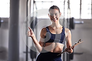 Thumbs up, personal trainer and fitness coach with gym clipboard to monitor health, weight loss and muscle growth