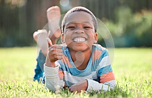 Thumbs up, portrait of black boy and lying on grass in a nature park with a lens flare. Good news or thank you, success