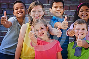 Thumbs up to another great year at school. a diverse group of children showing thumbs up outside.