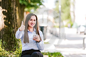 Thumbs up by young beautiful businesswoman who use cellphone outdoor