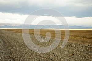 Thunderclouds over the gravel road and the endless autumn steppe stretching towards the snow-capped mountains