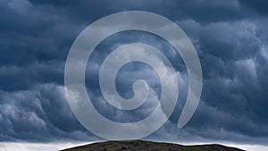 Thunderstorm over a hill on a hot summer day. Heavy leaden blue rain clouds low above the ground