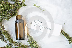 Thyme essential oil bottle with thyme herb twigs and label on concrete background, spa essential oil bottle